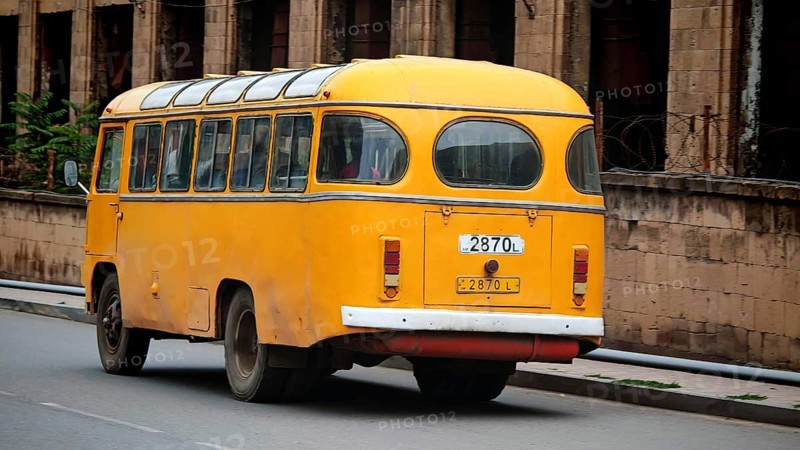 A yellow retro bus passes an old brick building along the road, Armenia