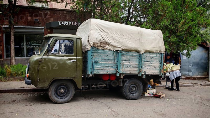 A vintage truck with a tarp on a road surrounded by trees, Armenia