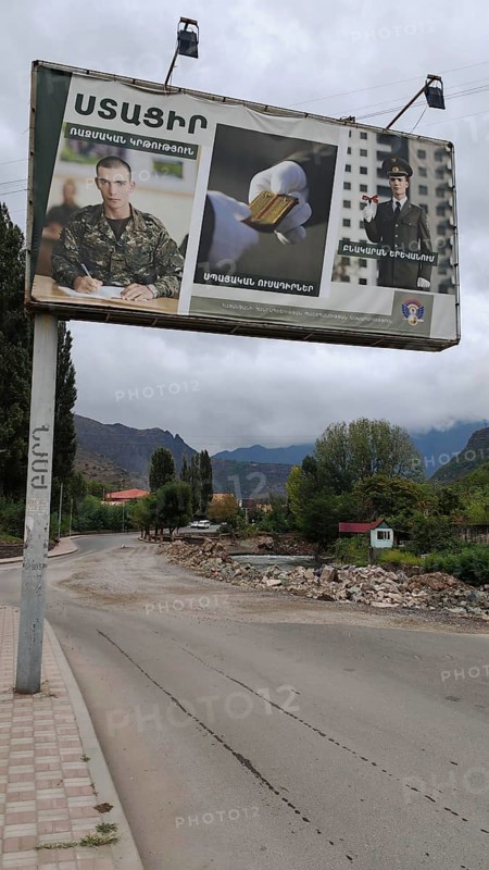 A large advertising poster on the side of the road, army looking for soldiers with mountains in the background, Armenia
