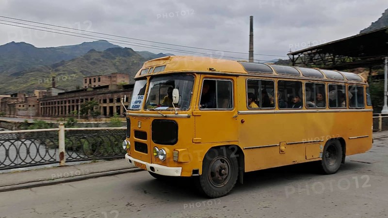 A yellow retro bus drives through an industrial area in a mountainous landscape, Armenia