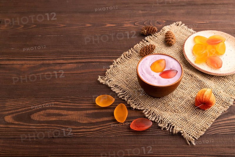 Purple Yogurt, with jelly candy on brown wooden background and linen textile, side view, copy space, minimalism