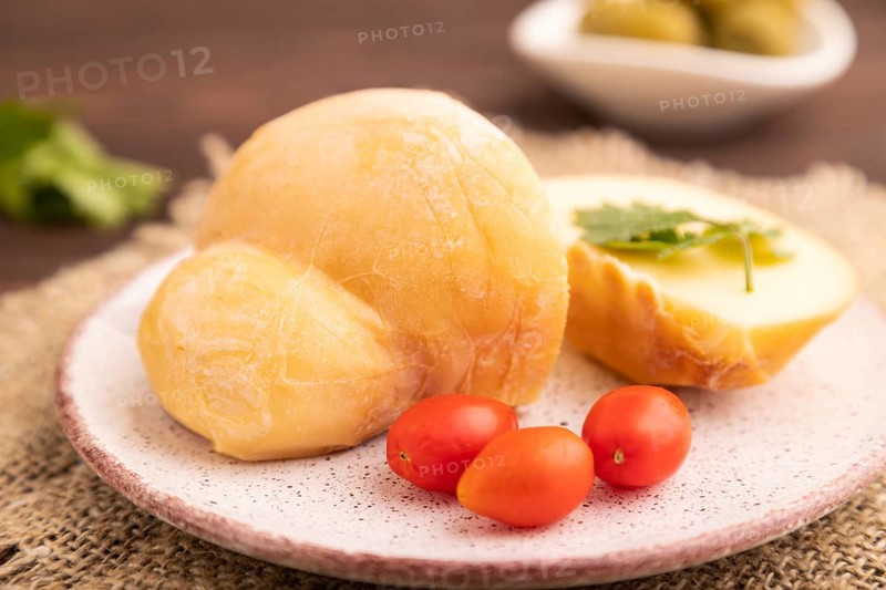 Smoked Mozzarella cheese, with tomatoes and olives on brown wooden background and linen textile, side view, close up, selective focus