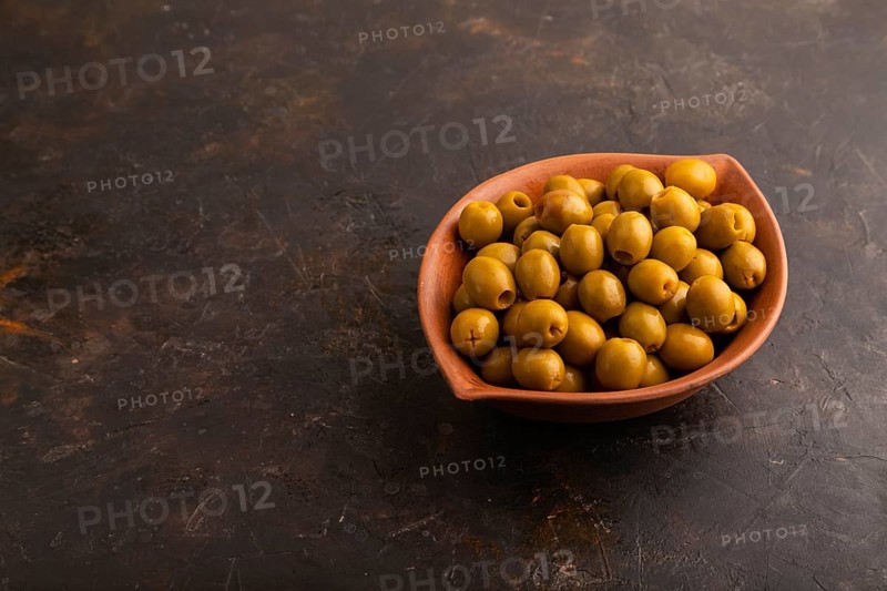 Fresh green olives in ceramic clay bowl on black concrete background. side view, copy space