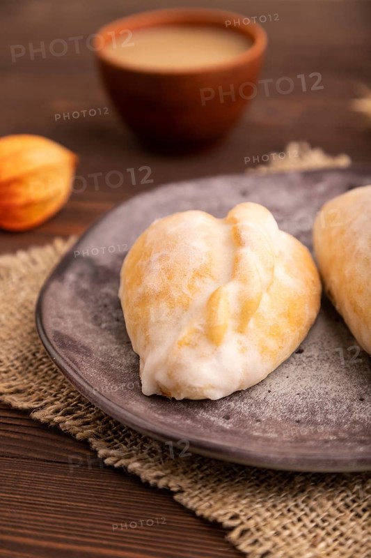 Glazed Pies with Cowberry jam on brown wooden background and linen textile, cup of coffee, side view, close up, selective focus