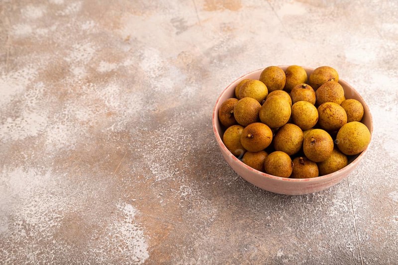 Ripe Longan in ceramic bowl on brown concrete background, side view, copy space, minimalism