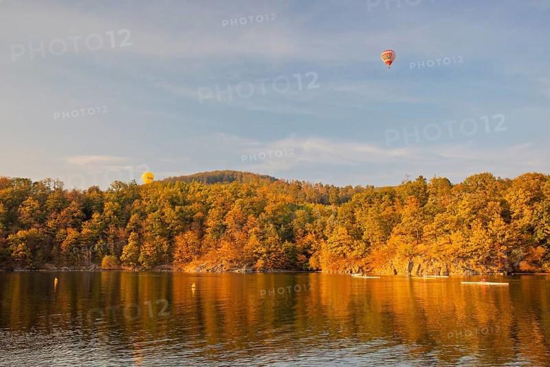 Hot air balloons over the Brno Reservoir (Brnenská prehrada) on the Svratka River on a sunny autumn day. Four rowing boats and a motorboat can be seen. The reservoir is located northwest of the city of Brno in the Czech Republic