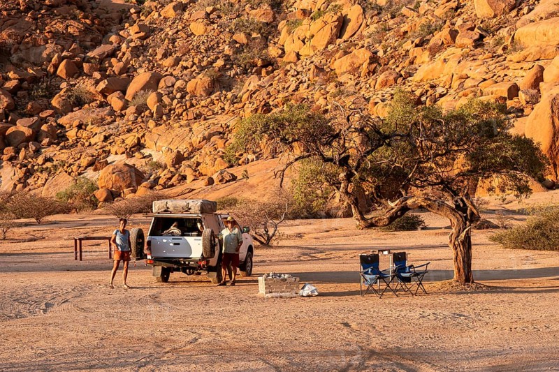 Camping in the Spitzkoppe desert under a tree next to a vehicle, surrounded by impressive rock formations, Spitzkoppe, Namibia