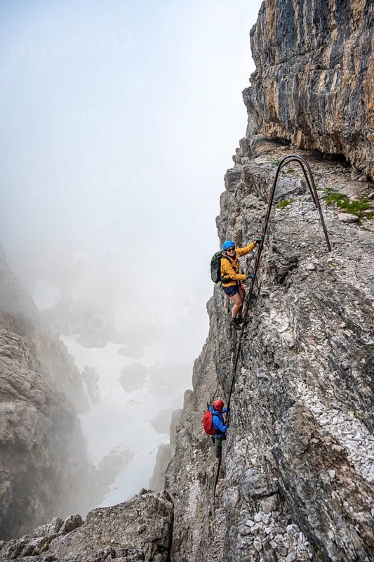 Mountaineers on a ladder on the Via Ferrata Oliva Detassis via ferrata in fog, rocky mountain peaks and mountain landscape, Brenta Mountains, Parco Naturale Brenta-Adamello, Trentino, Italy