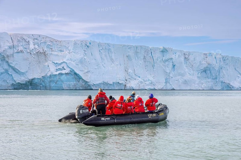 Eco-tourists in Zodiac boat from Poseidon Expeditions looking at Brasvellbreen glacier wall debouching into the Barents Sea, Svalbard / Spitsbergen