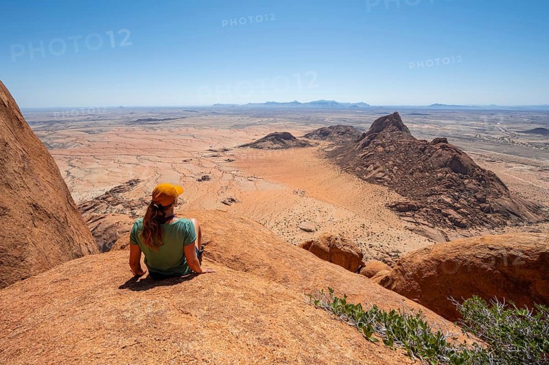 Woman sitting on rocks and enjoying the view over the barren desert landscape of Spitzkoppe, Spitzkoppe, Erongo, Namibia