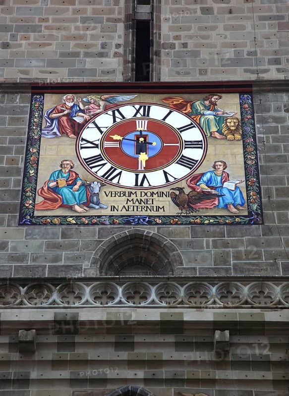 The picture shows the striking tower clock of the Black Church, Biserica Neagr, in Brasov, Brasov, Romania. The city's landmark is home to an ornate clock face that combines both religious symbols and a Latin inscription. Characterised by the four evangelists, the clock face is surrounded by the four canonical evangelists, each depicted with their traditional symbols: Matthew (man/angel), Mark (lion), Luke (bull) and John (eagle)