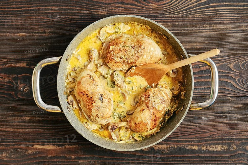 Top view of homemade creamy chicken thighs with mushroom sauce in skillet, served with herbs on rustic wooden surface