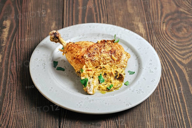 A chicken leg cooked and placed on a round plate. The dish features a creamy mushroom sauce and is garnished with green herbs