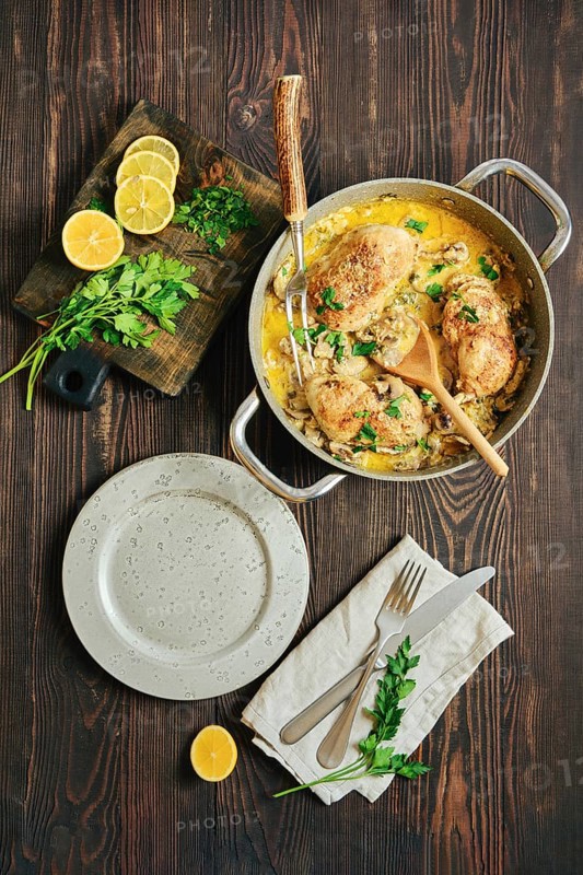 Overhead view of creamy chicken thighs with mustard mushroom sauce and fresh parsley and lemon on rustic table