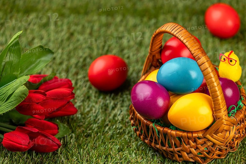 A basket of colorful Easter eggs next to flowers in a meadow
