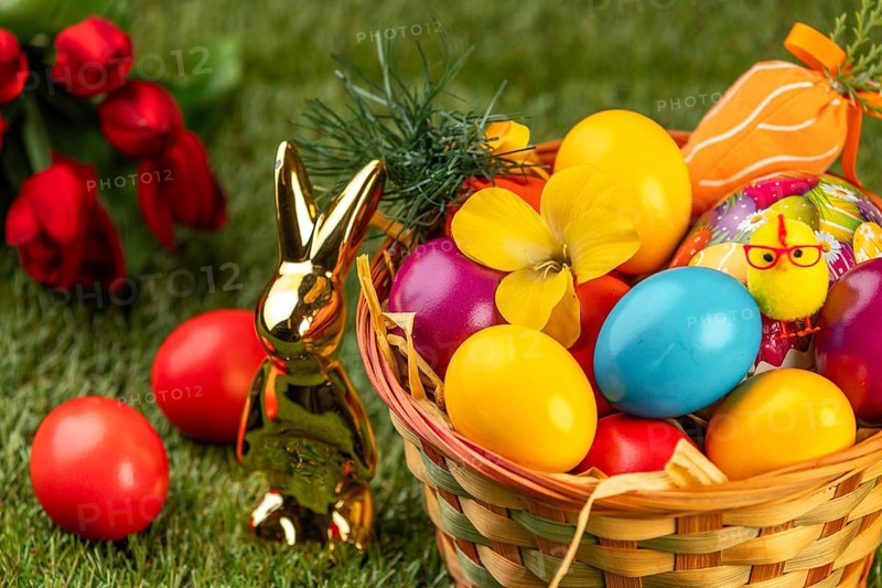 A basket with colorful Easter eggs and a rabbit statue on grass