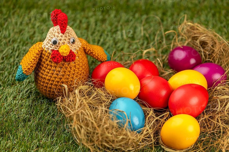 Crocheted chicken and colorful easter eggs in a nest on grass