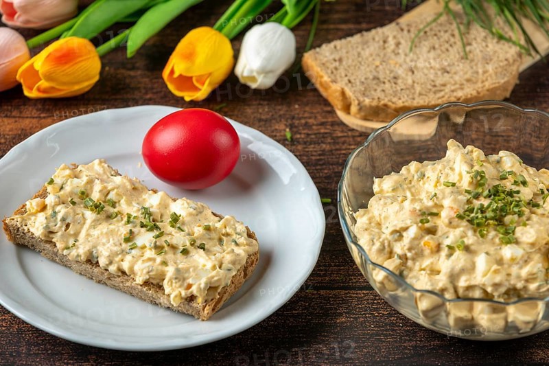 Egg salad on a plate with bread, surrounded by fresh ingredients and flowers
