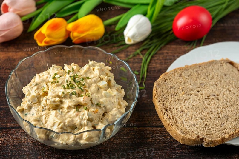 Egg salad next to a slice of bread and tulips, on rustic wooden table