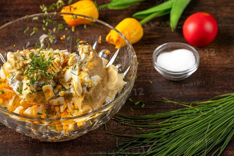 Chives fall into a bowl with ingredients for egg salad on wooden table