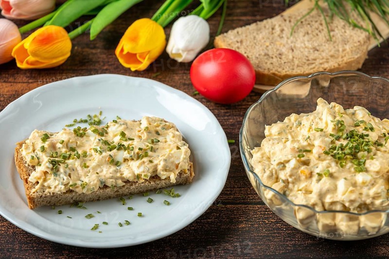 Slice of bread with egg salad on plate, with fresh herbs, tulips in the background
