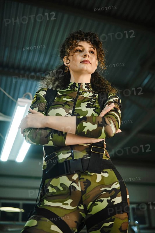 Low angle view at a woman standing with her arms crossed in a camouflage suit