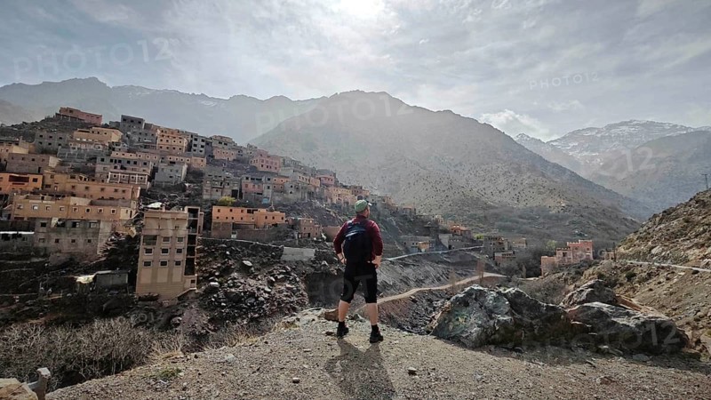 A hiker with backpack stands in front of a mountainous village in sunny weather, Atlas Mountains, Morocco