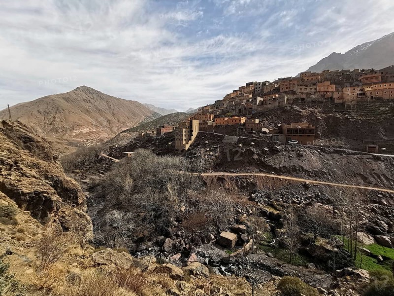 A village on a dry hill with sparse vegetation under a cloudy sky, Atlas Mountains, Morocco