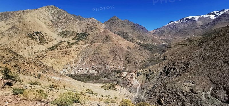 Breathtaking view of a village in a rocky mountain landscape with snow-covered grips under clear sky, Atlas Mountains, Morocco