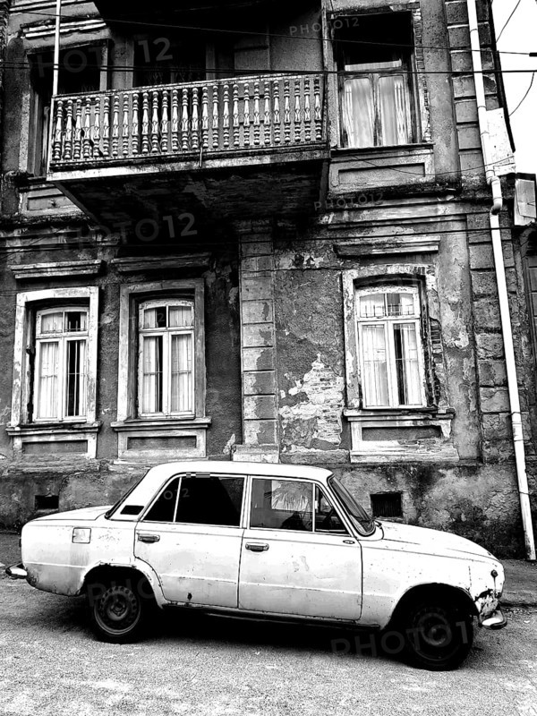 Monochrome, vintage car standing in front of a Nostaligian building with a distinctive balcony, Georgia