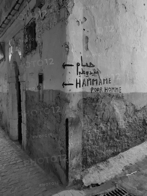 Dilapidated wall with graffiti and references to a hammam in a narrow alley, monochrome, old town of Essaouira, Morocco