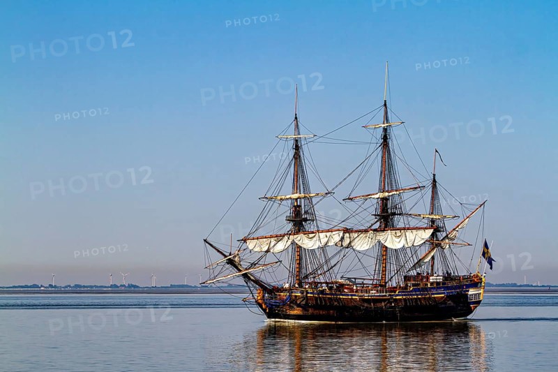 A traditional sailing ship with full sails on calm water under clear blue skies, an old historic sailing ship