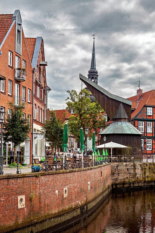 Timber crane and half-timbered houses with a tower on the riverbank under a dramatic sky, The old town of Stade