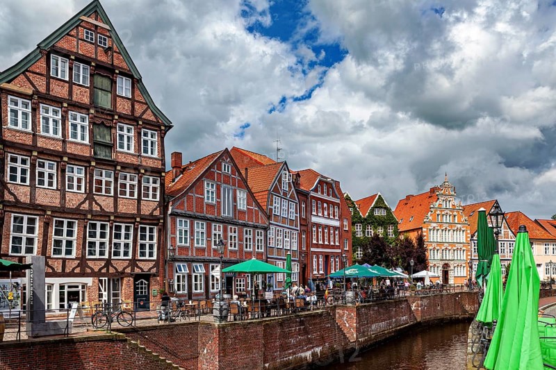 Half-timbered facades and terraces on the river with cyclists and cloudy sky, The old town of Stade