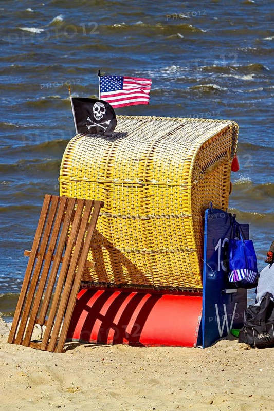 A single yellow beach chair on the beach with American and pirate flag in the wind, beach chairs on the beach in Cuxhaven