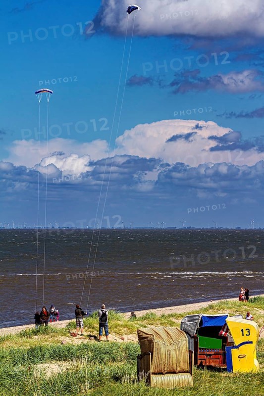 Beach chairs by the sea with people and kites in the sky under blue sky and clouds, beach chairs on Cuxhaven beach