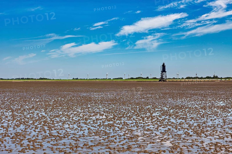 A lighthouse in the Wadden Sea with wind turbines on the horizon under a blue sky, Die Kugelbake von Cuxhaven