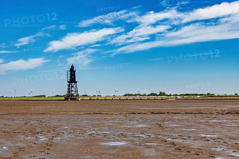 A lighthouse in the Wadden Sea with wind turbines in a vast, cloudy landscape, The Kugelbake von Cuxhaven