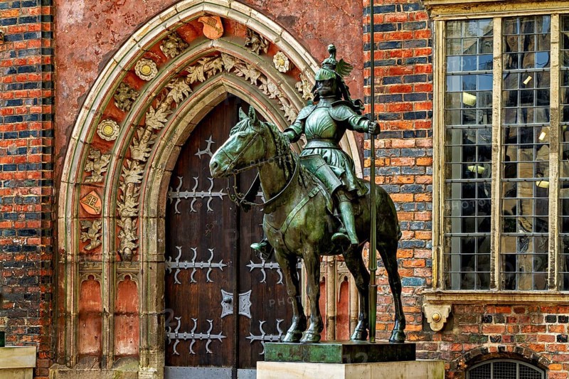 An equestrian statue in front of a Gothic building with richly decorated archway and red bricks, equestrian statue in Bremen