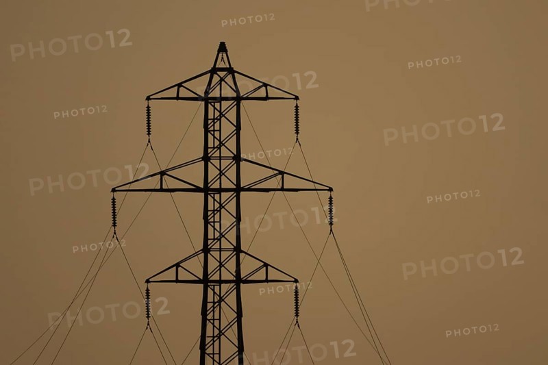 Electricity pylon and power lines silhouette at sunset, England, United Kingdom