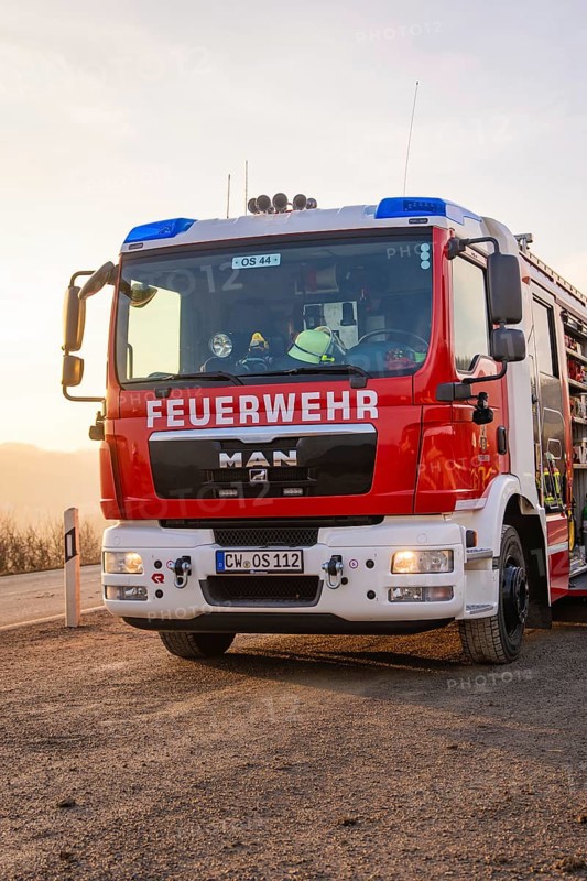 A MAN fire engine with the inscription 'FIRE DEPARTMENT' is parked on the side of the road when the sun rises, fire department practice on the Hermann Hesse Railway, Ostelsheim, Calw district, Germany