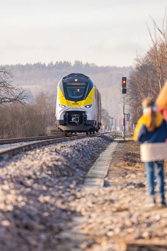 A yellow train travels on rails through a rural area with trees and people on the side of the road, fire department exercise at the Hermann Hesse Railway, Ostelsheim, Calw district, Germany