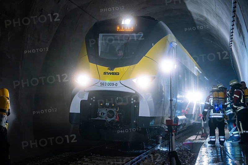 A train goes through an illuminated tunnel with firefighters in the background, fire department exercise on the Hermann Hesse Railway, Ostelsheim, Germany