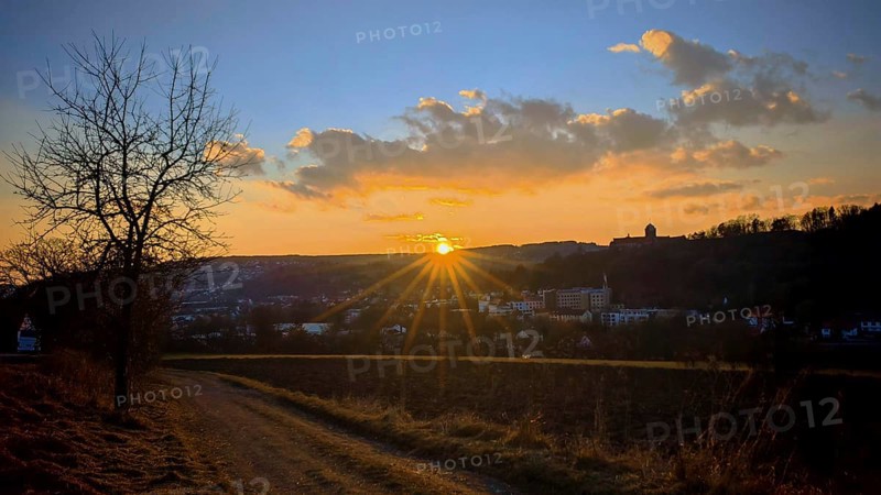 An idyllic sunset over an urban landscape with a path that leads through fields, a view towards Kronach, Frankenwald nature park Park