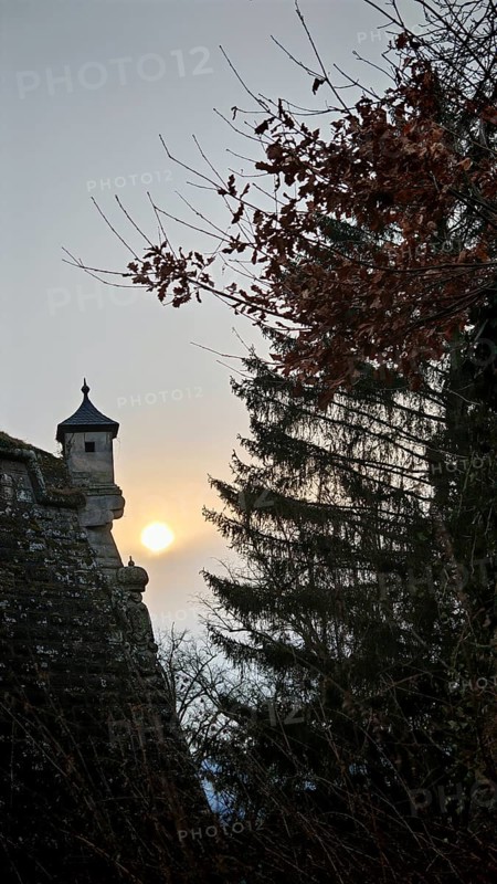A castle tower, bay window of a fortress wall rising into the sky, surrounded by trees at sunset, Franconian Forest nature park Park