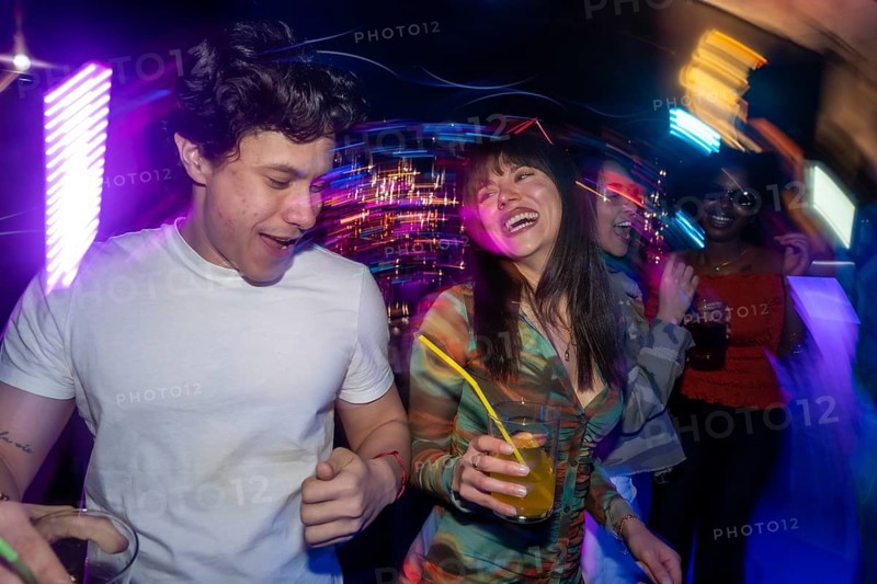 Young diverse people are dancing and interacting in a discotheque, surrounded by colorful neon lights and motion blur, enjoying a night out with refreshing cocktails