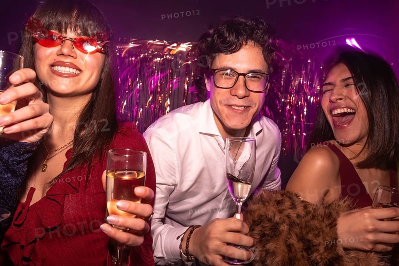 Young friends enjoying a vibrant night out with drinks, smiling and laughing under club lights, sharing moments of happiness and celebration at a lively social event
