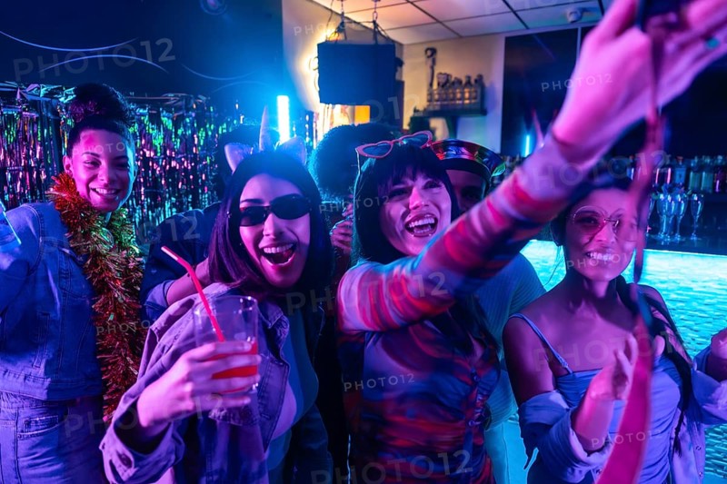 Young diverse friends enjoying a lively nightclub party, smiling, dancing, and posing for a selfie, illuminated by colorful neon lights and creating a festive atmosphere