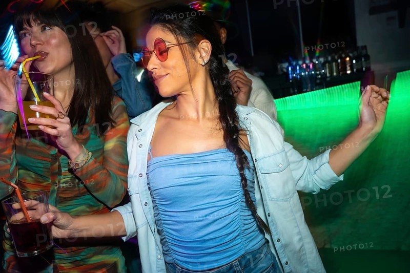 Young women enjoying nightlife, dancing and drinking cocktails with neon light reflections at a lively nightclub, creating a vibrant atmosphere of fun and celebration