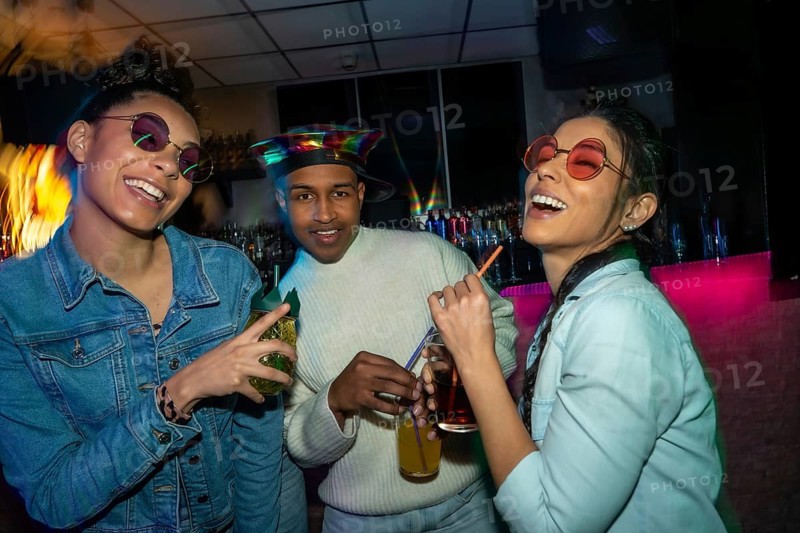 Diverse group of young people socializing at a bar, laughing and holding cocktails under colorful lights, capturing the fun and excitement of a night out